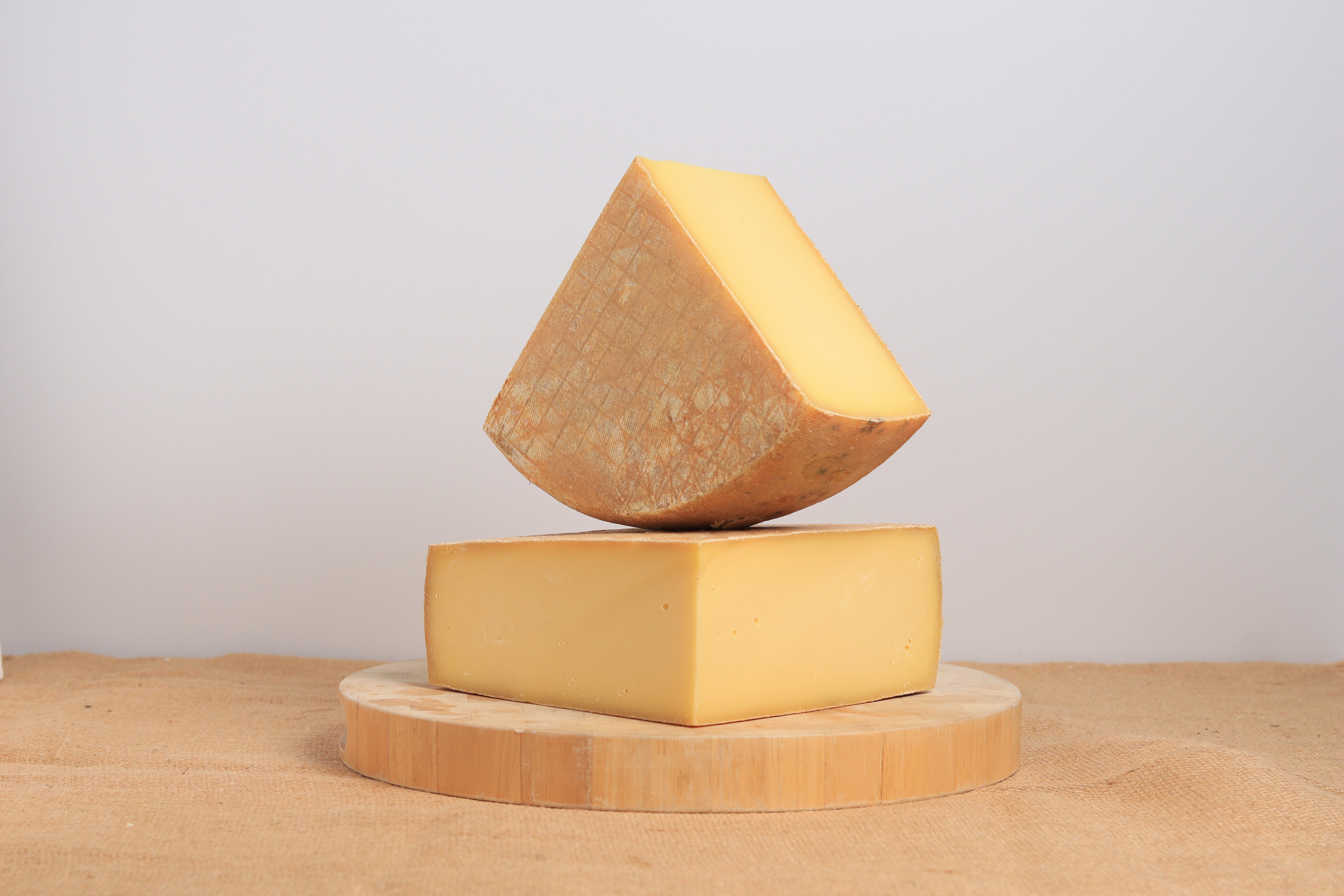 2 large pieces of an alpin-style cheese, one on top of the other, showing the smooth light yellow interior and orangey skin