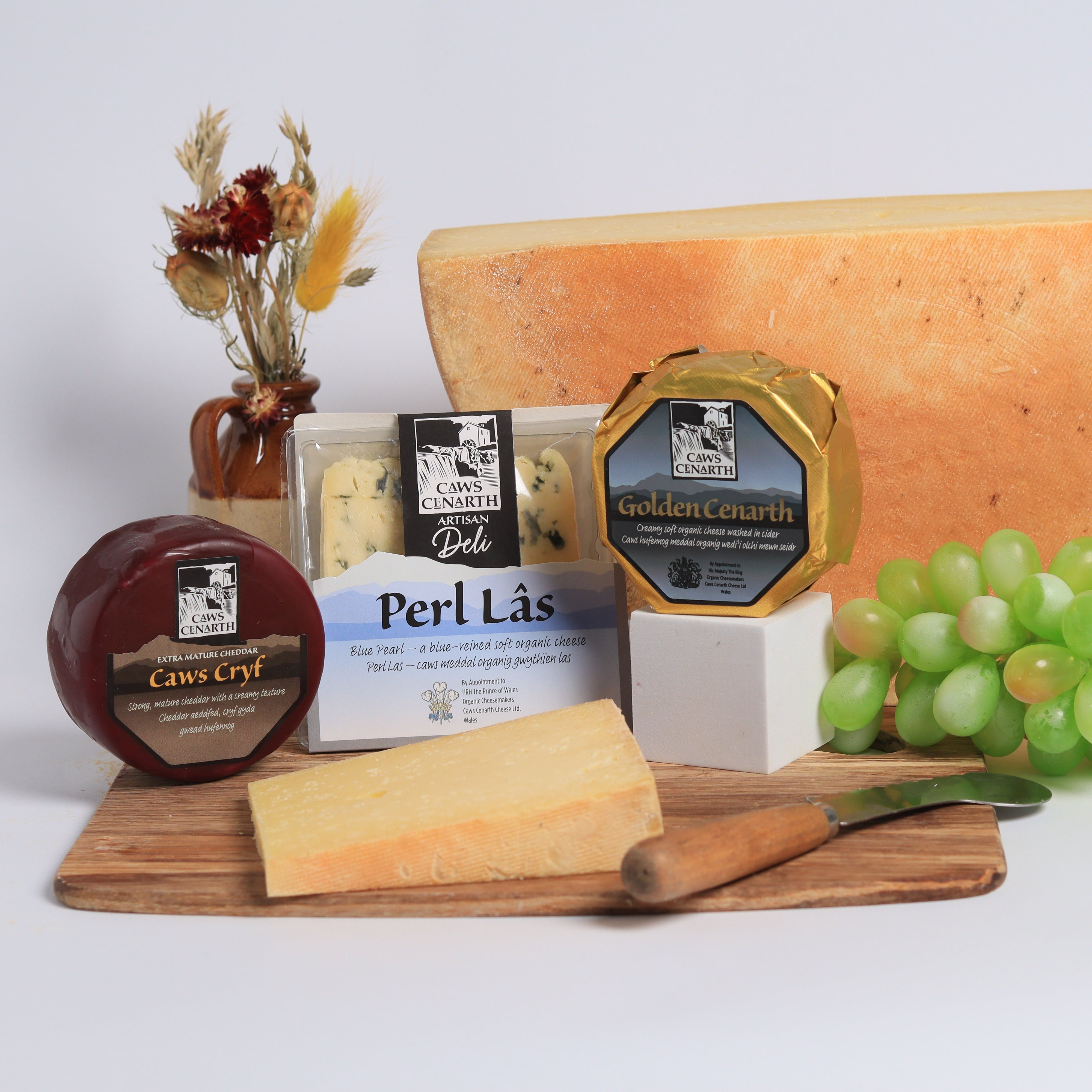 Assorted cheeses on a wooden board with grapes and a knife on a white background