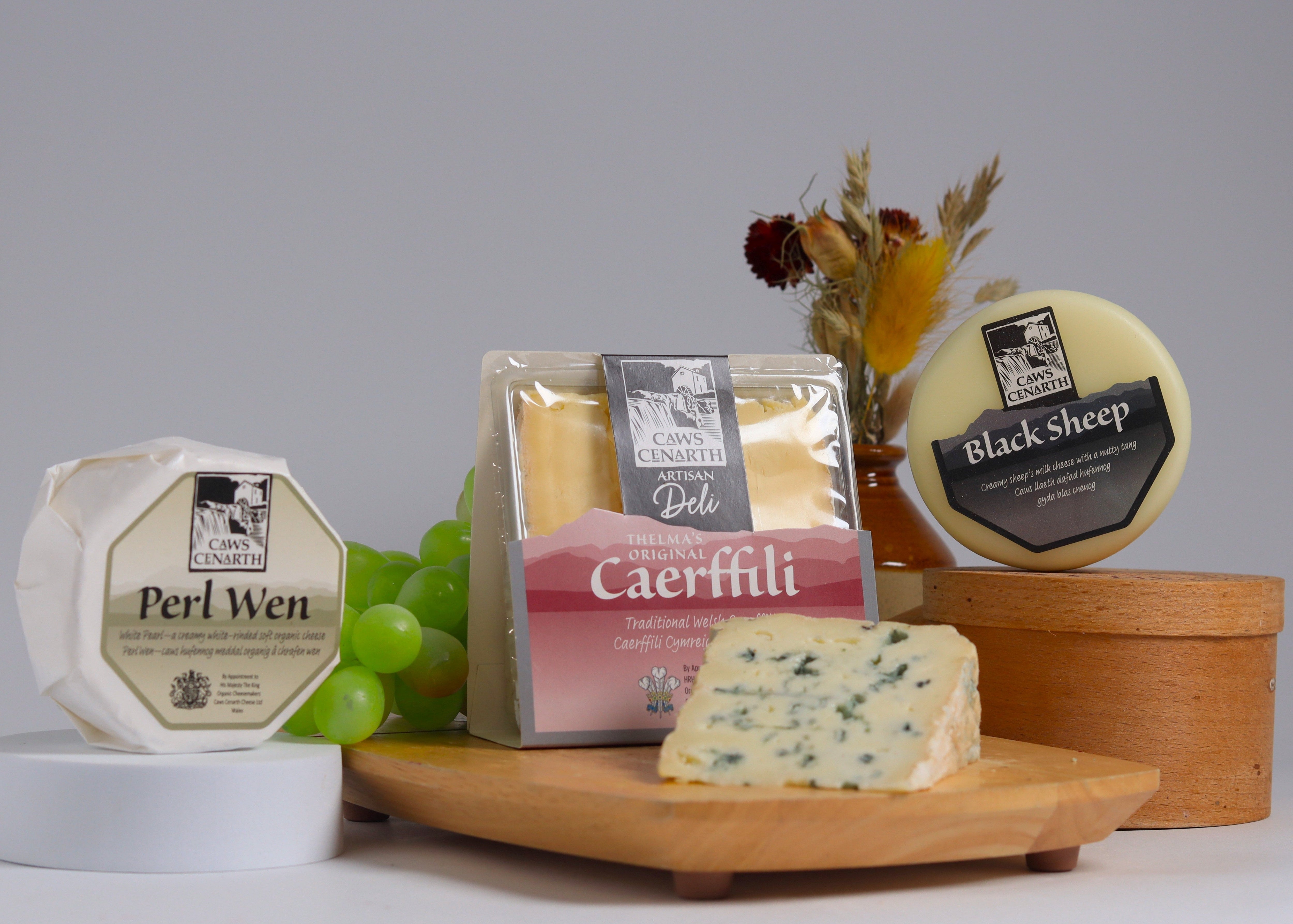 4 assorted Caws Cenarth cheeses on a wooden board with a grey background